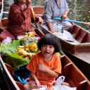 A girl enjoying Thai dessert while her grandma is selling bananas at Damnoen Saduak floating market. Enjoy delicious local snacks and fruits on our floating market tour from Bangkok.